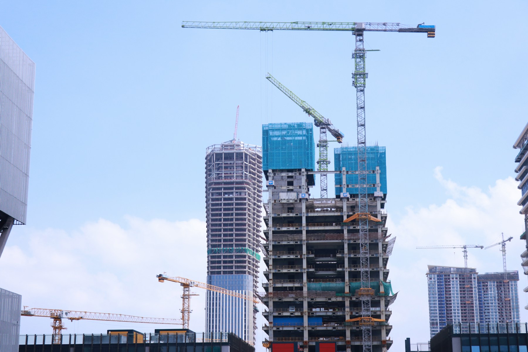 Concrete high-rise buildings under construction with tower cranes and blue safety screens